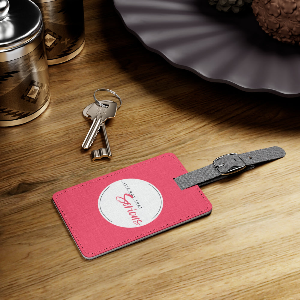 Pink luggage tag with a gray strap on a wooden surface with keys and a container.