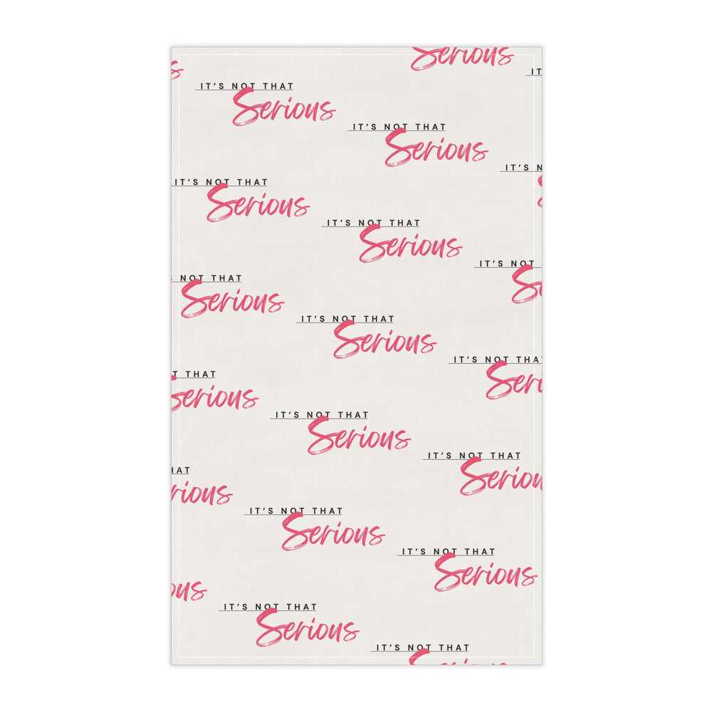 A white cotton tea towel with red text pattern hanging on a white shelf, with kitchen items and a plant in the background.