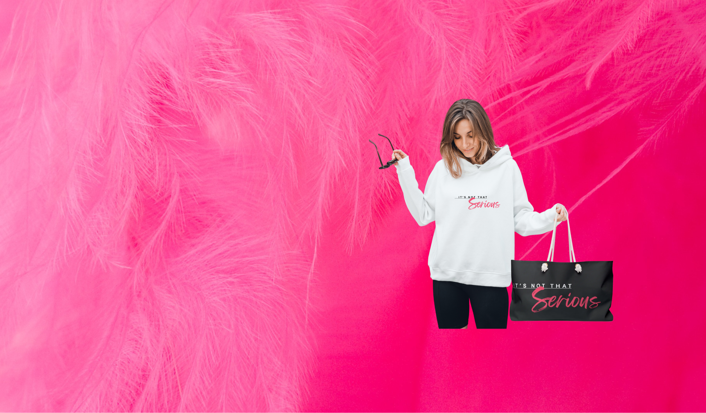 Women in a white It's Not That Serious logo hoodie with a branded weekender bag with a hot pink feather background
