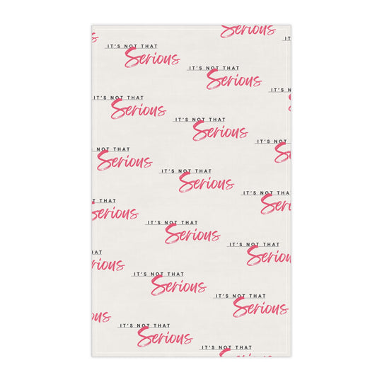 A white cotton tea towel with red text pattern hanging on a white shelf, with kitchen items and a plant in the background.