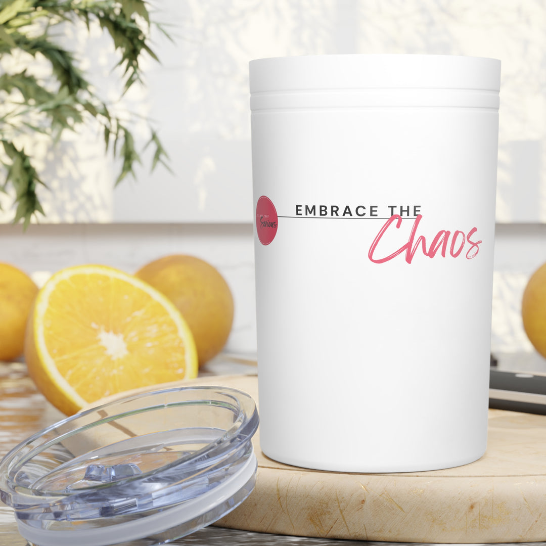 White tumbler with 'Embrace the Chaos' text on a table with lemons and a plant in the background