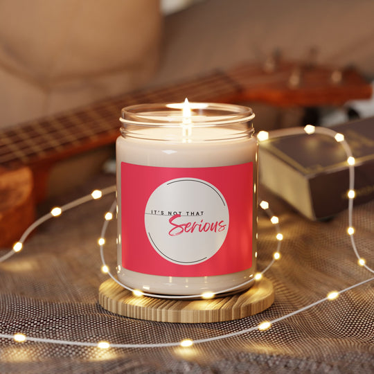 Candle in a jar with a pink label on a wooden surface with string lights and a guitar in the background