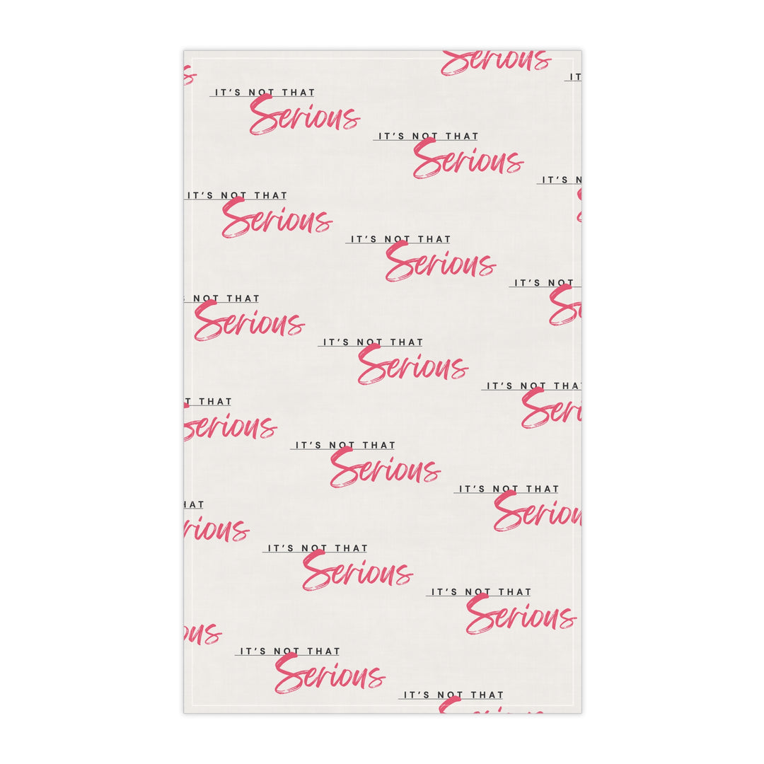 A white cotton tea towel with red text pattern hanging on a white shelf, with kitchen items and a plant in the background.