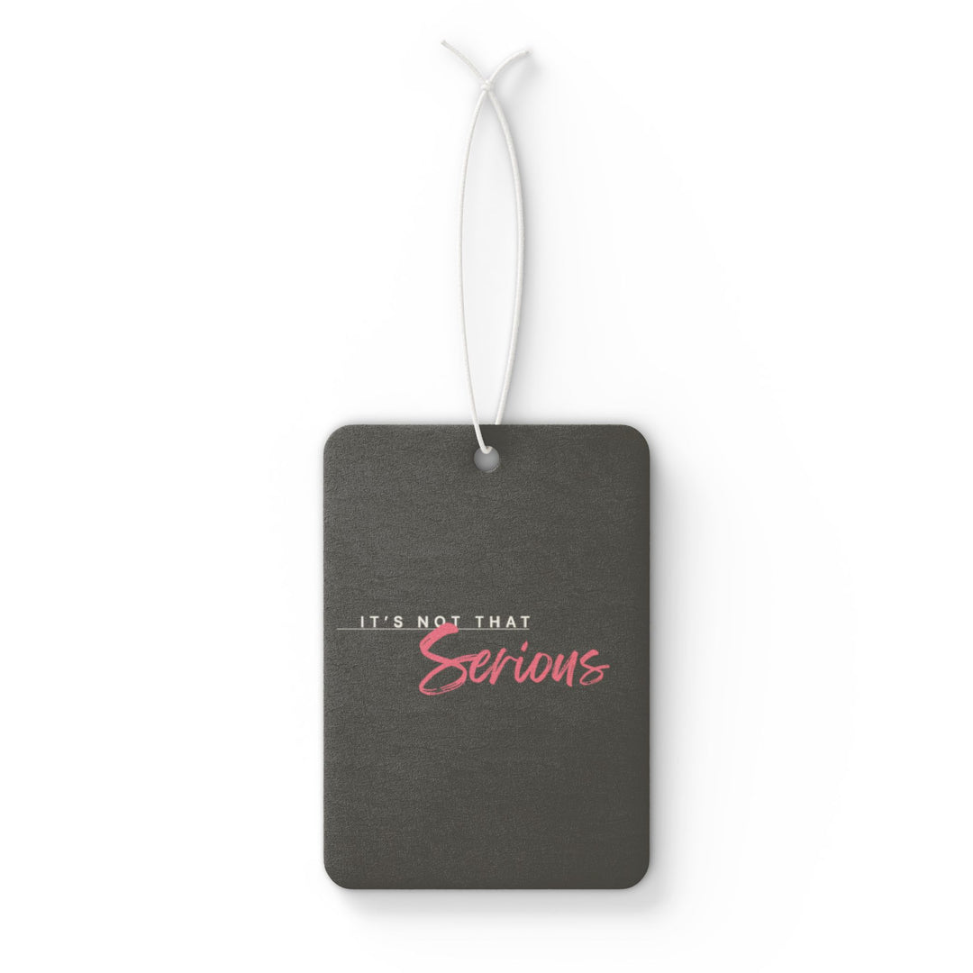 A gray car air freshener with pink text that reads 'It's Not That Serious' hanging by a white string.