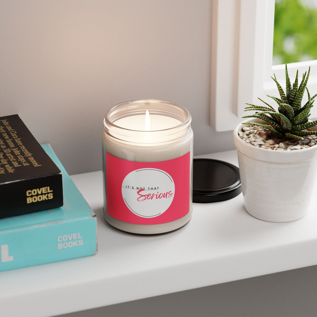 Candle with a pink label on a shelf with books and a plant