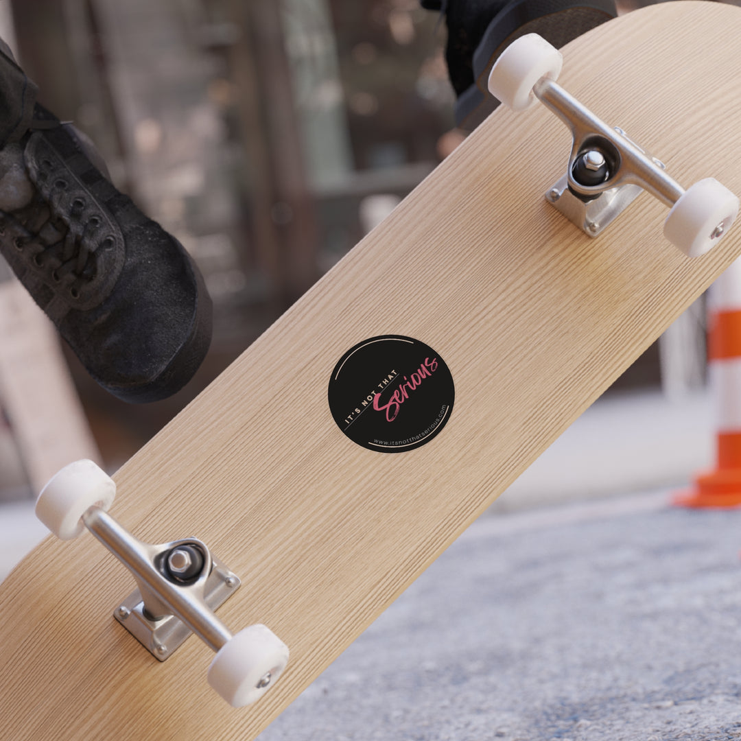 A sticker with the text 'It's Not That Serious' placed on a wooden skateboard surface, partially visible white wheels and a black shoe in the background.