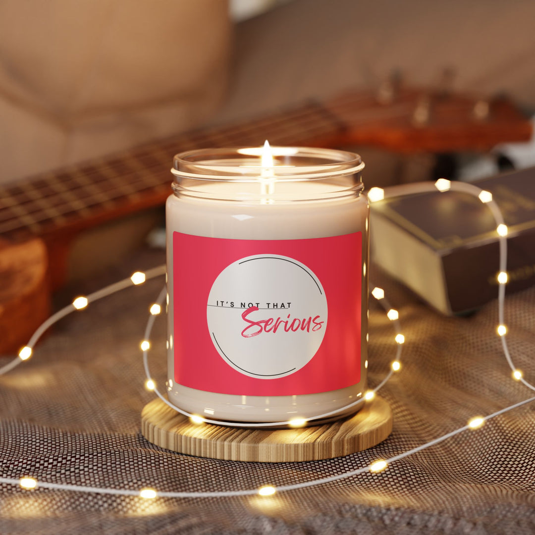 Candle in a jar with a pink label on a wooden surface with string lights and a guitar in the background