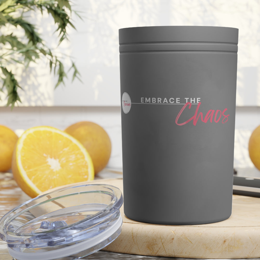 Gray tumbler with 'Embrace the Chaos' text on a wooden surface with oranges in the background