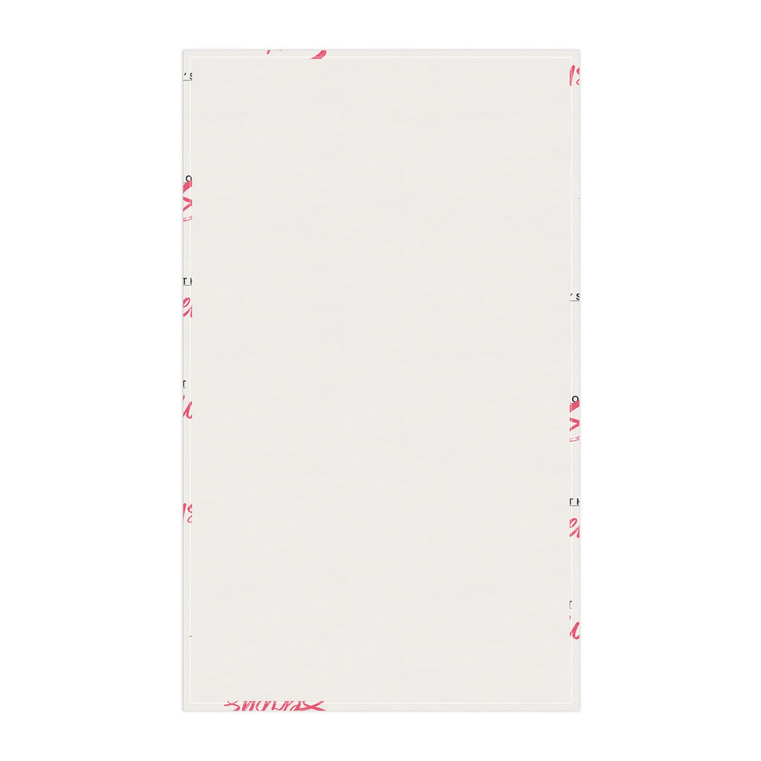 A white cotton tea towel with red text pattern hanging on a white shelf, with kitchen items and a plant in the background.