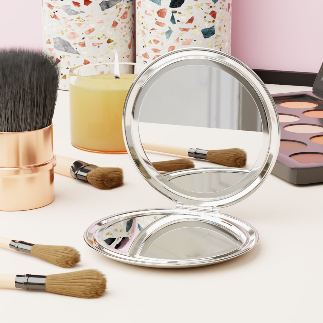 Round silver mirror with makeup brushes and products on a light surface