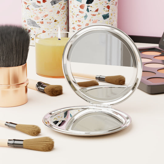 Round silver mirror with makeup brushes and products on a light surface