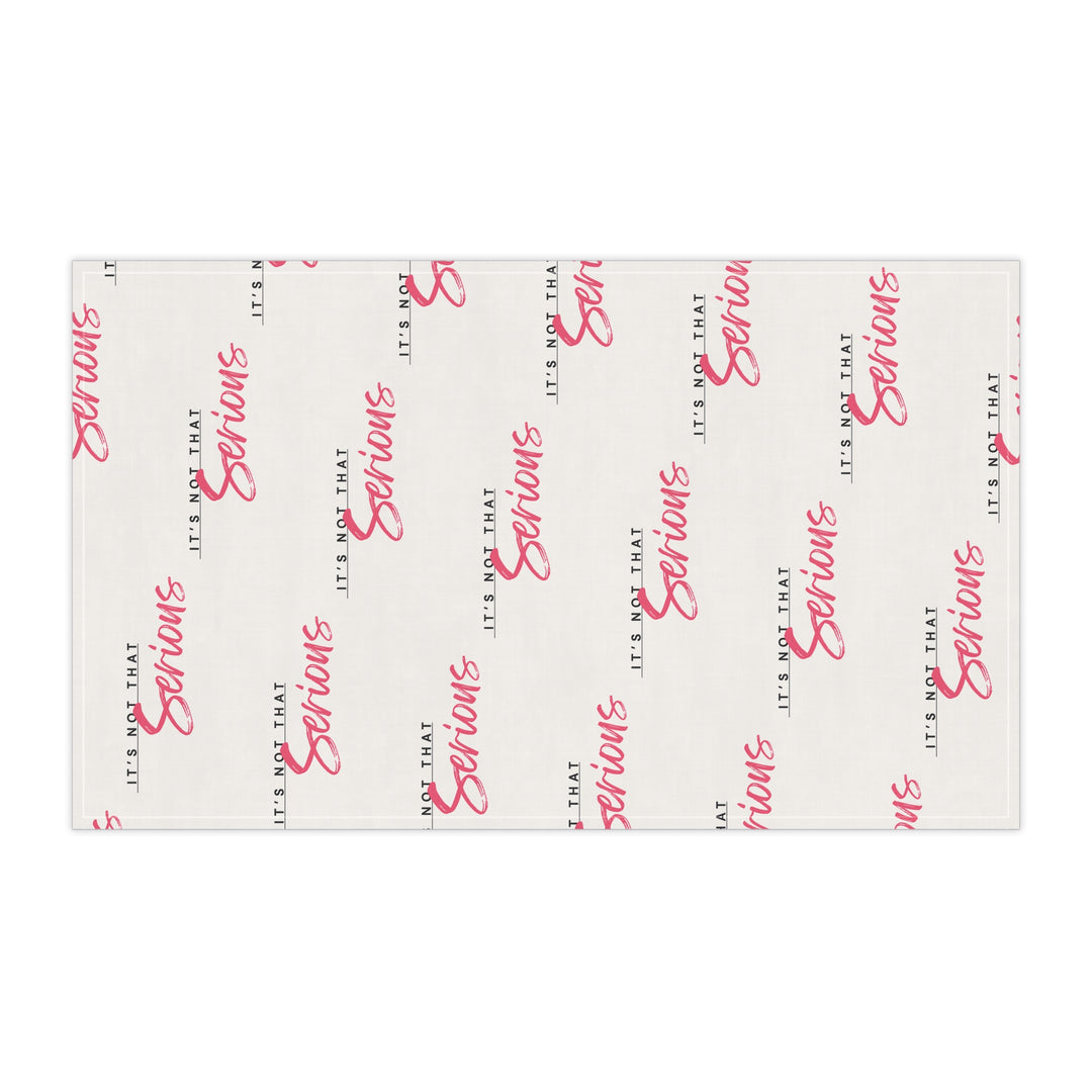 A white cotton tea towel with red text pattern hanging on a white shelf, with kitchen items and a plant in the background.