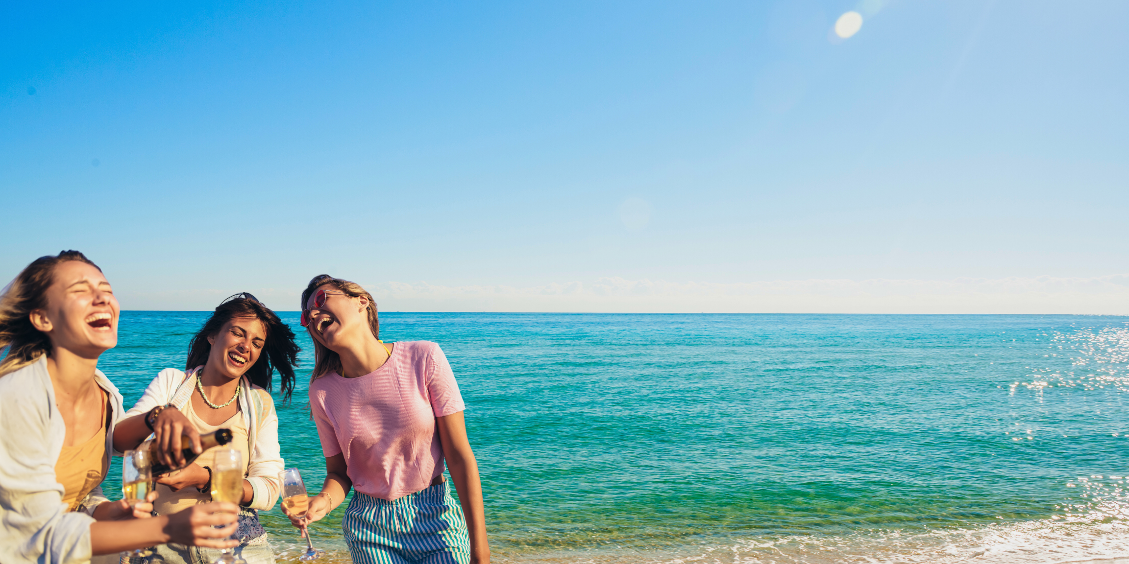 Three women drinking champagne on the beach laughing