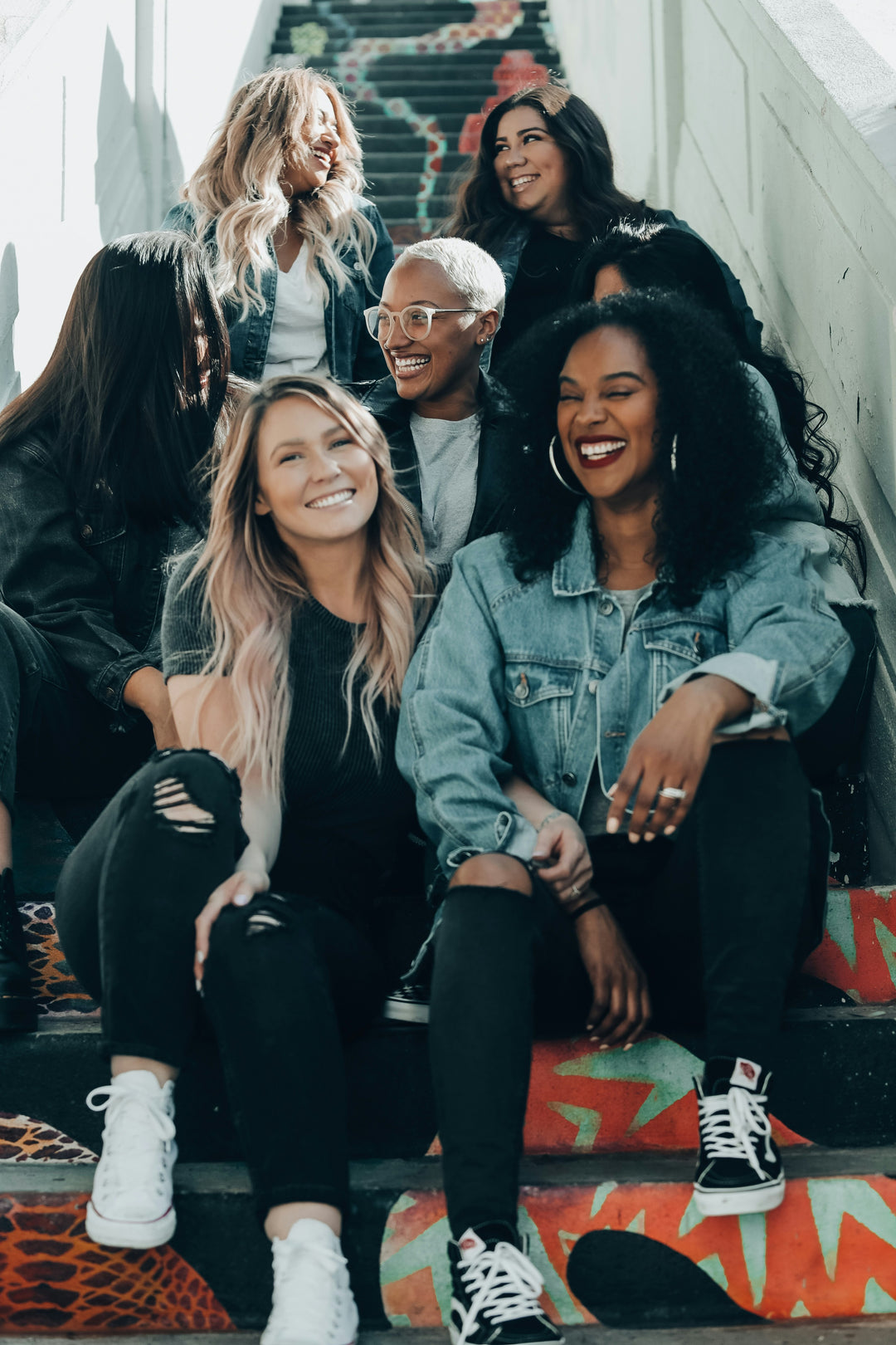 A group of young adults sitting and standing on a staircase, smiling and interacting with each other.